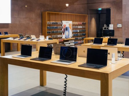 Téléchargez les photos : Paris, France - 23 déc. 2024 : Un Apple Store avec des ordinateurs portables MacBook sur des tables en bois, avec des étagères de coques d'iPhone et d'autres accessoires Apple affichés en arrière-plan. - en image libre de droit