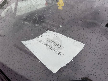 Ein Zettel mit Restitution Destination CEO auf der Windschutzscheibe eines Autos, bedeckt mit Regentropfen, zeigt einen Regentag und Tröpfchen auf dem Glas - Autohaus