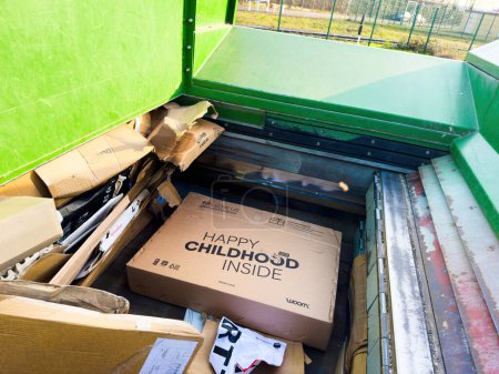 Foto de París, Francia - 1 de marzo de 2024: Una papelera de reciclaje verde llena de cajas de cartón y materiales de embalaje, incluida una caja etiquetada como Happy Childhood Inside "que indica la gestión organizada de residuos. - Imagen libre de derechos