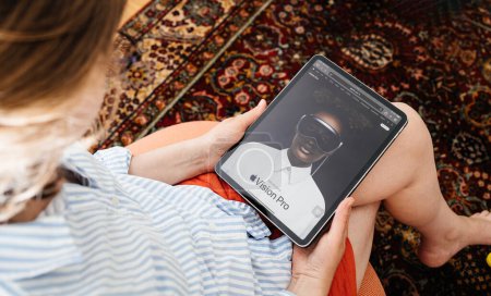 Photo for London, United Kingdom - Jun 11, 2023: A woman sits comfortably in her living room, reading about the Apple Vision Pro mixed-reality headset on her iPad Pro, exploring the features shown on the screen - Royalty Free Image