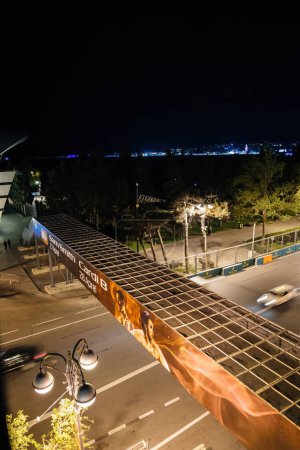 Foto de Bakú, Azerbaiyán - 3 de mayo de 2019: Vista nocturna de una pancarta promocional para los conciertos de Sam Smith y Cardi B en un puente en Bakú, con autos borrosos pasando por debajo y luces de la ciudad visibles en el fondo - Imagen libre de derechos