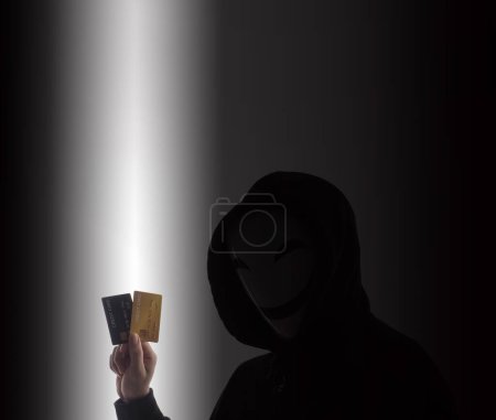 Téléchargez les photos : Un pirate et des cartes de crédit en main. Représenter les données personnelles des cartes de crédit volées par un homme anonyme en chemise Black hood. Sécurité des données des cartes de crédit et cybercriminalité numérique. Transection d'argent non sécurisée. - en image libre de droit