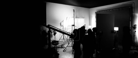 Téléchargez les photos : Images en silhouette de réalisation de ou dans les coulisses de la production vidéo qui a produit dans le studio de cinéma qui comprennent tous les équipements pro lumière et caméra et équipe de tournage professionnelle avec réalisateur - en image libre de droit