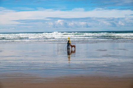 Mirando las olas del océano una mujer y su perro en Canon Beach estado de Oregon. 