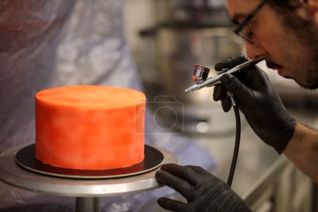 Téléchargez les photos : Cuisinier préparer un gâteau rouge givré en utilisant la brousse d'air - en image libre de droit