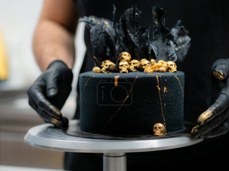 Foto de Pastelero terminando horror negro muertos pastel de cumpleaños decoración con cráneos comestibles de oro y velas de papel de arroz negro - Imagen libre de derechos