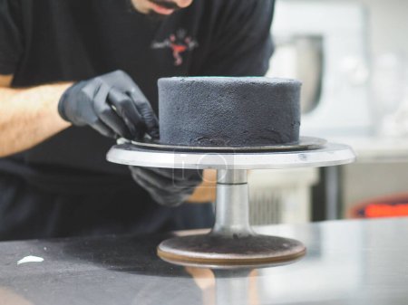 Photo for Chef pastry cook decorating and preparing a black matte spongy sprayed frosted cake for birthday - Royalty Free Image