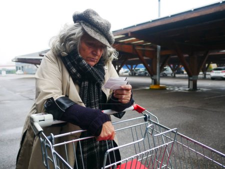 Téléchargez les photos : Hispanique jeune femme adulte poussant chariot lecture main écrit épicerie liste d'achats dans le parking dans le grand supermarché magasin - en image libre de droit