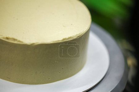 Photo for Pastry chef using spatula scraper to smooth green pistachio buttercream frosted cake - wedding cake preparation - Royalty Free Image