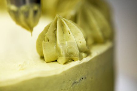 Téléchargez les photos : Pâtisserie chef designer faire tourbillons avec sac de tuyauterie remplissage à la crème pistache sur gâteau au chocolat vert givré en couches - en image libre de droit