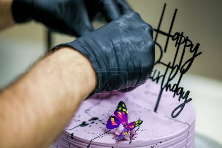 Téléchargez les photos : Pâtissier garniture lilas givré anniversaire gâteau stratifié fait à la main avec signe de naissance heureux texte et papillons topper - en image libre de droit