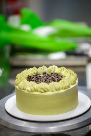 Téléchargez les photos : Pâtissier saupoudrer le dessus de gâteau au chocolat givré en couches vertes avec de petits morceaux de pistacchio et de chocolat noir - en image libre de droit