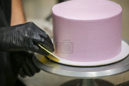 Photo for Pastry chef using spatula and scraper smoothing levelling layered lilac buttercream frosted cake - wedding cake preparation - Royalty Free Image