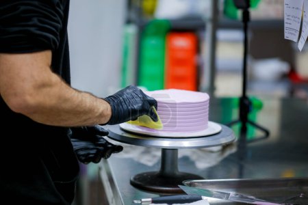 Téléchargez les photos : Chef pâtissier utilisant grattoir spatule pour lisser lilas rose beurre crème gâteau givré - préparation gâteau d'anniversaire - en image libre de droit