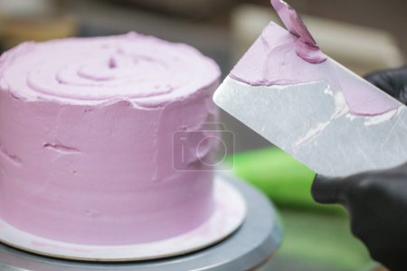 Photo for Pastry chef using spatula and scraper smoothing levelling layered lilac buttercream frosted cake - wedding cake preparation - Royalty Free Image