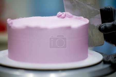 Photo for Pastry chef using spatula scraper to smooth lilac pink buttercream frosted cake - birthday cake preparation - Royalty Free Image