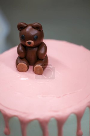 Photo for Cake designer finishing decoration on frosted dripping icing pink white cake handmade bear edible topping - Royalty Free Image