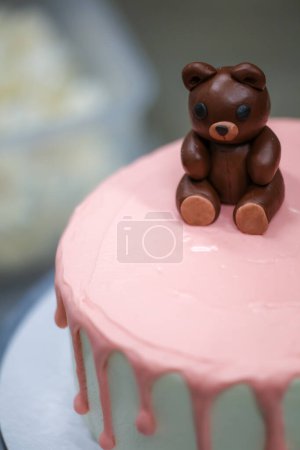 Photo for Cake designer finishing decoration on frosted dripping icing pink white cake handmade bear edible topping - Royalty Free Image