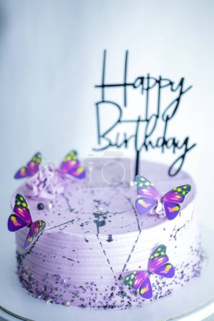 Téléchargez les photos : Gâteau lilas glaçage stratifié givré avec signe joyeux anniversaire et papillons topper sur pied sur fond blanc - colorisation des aliments sucrés noir et violet - en image libre de droit