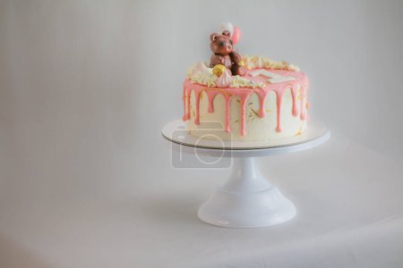 Photo for Frosted dripping icing pink white cake with handmade bear topping on stand on white background for one year old baby girl - Royalty Free Image