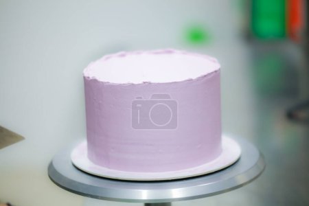 Téléchargez les photos : Chef pâtissier utilisant spatule et grattoir lissage nivellement couches lilas beurre crème gâteau givré - préparation gâteau de mariage - en image libre de droit