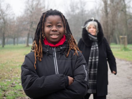 Photo for A happy young black girl walk with granny in a park in cold weather wearing sportswear.Afro dreadlock hairstyle. - Royalty Free Image