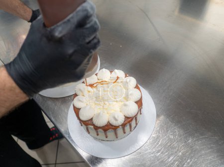 Photo for Chef pastry baker preparing salty caramel frosted dripping white cakes with meringues on top - Royalty Free Image