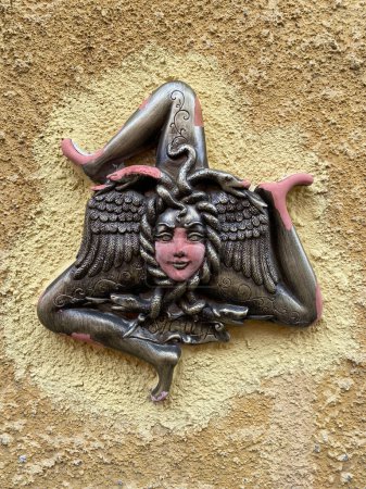 Téléchargez les photos : Sculpture traditionnelle en céramique de Trinacria, symbole à trois pattes de la Sicile. Gros plan sur un mur beige. - en image libre de droit