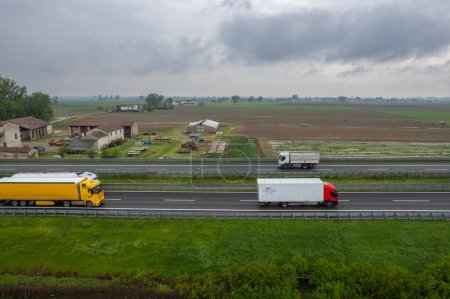 Photo for Piacenza, Italy - April 2023 Cargo trucks and cars in the motorway a1 autostrada del sole aerial point of view in between padain plain rural fields - Royalty Free Image