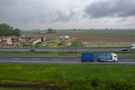 Photo for Piacenza, Italy - April 2023 Cargo trucks and cars in the motorway a1 autostrada del sole aerial point of view in between padain plain rural fields - Royalty Free Image