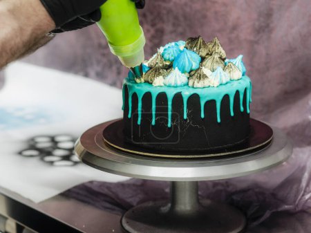 Photo for Frosted black painted cup cake with blue turquoise dripping and colored handmade meringue topping studio white isolated background - Royalty Free Image