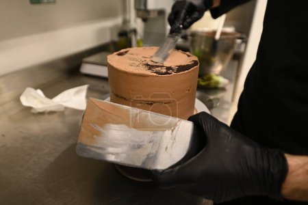 Foto de Pastelero suavizando la crema en una capa esmerilada pastel de chocolate negro en la cocina profesional de alta res imagen - Imagen libre de derechos