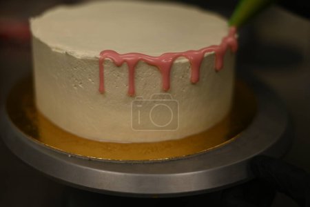Foto de Pastelero utilizando la bolsa de tuberías llena de crema de mantequilla para decorar un pastel de taza cremosa capas esmeriladas - Imagen libre de derechos