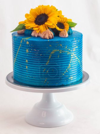 Atemberaubende Torte mit leuchtend blauem Zuckerguss, verziert mit frischen Sonnenblumen und Feigen, auf einem weißen Kuchenständer vor neutralem Hintergrund