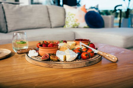 Foto de Quesos, frutas y verduras en una tabla de cortar de madera en un apartamento moderno - Imagen libre de derechos