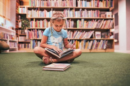 Photo for Primary schoolgirl doing homework in school library. Student learning from books. Pupil having fun studying interesting books. Back to school - Royalty Free Image