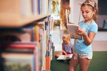 Schulmädchen auf der Suche nach Büchern zum Lesen in der Schulbibliothek. Schüler wählen Bücher zum Lesen aus. Von Büchern lernen. Zurück zur Schule. Grundschulbildung. Hausaufgaben machen