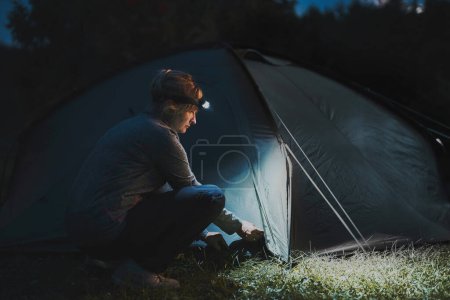Vacances d'été. Tente d'ouverture femme au camping le soir en utilisant une lampe frontale. Voyage d'été. Préparation du camping. Passer des vacances en plein air près de la nature
