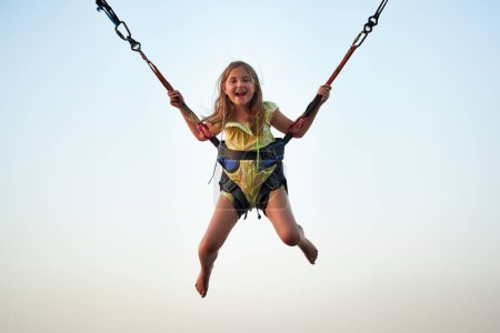 Foto de Bungee saltando al trampolín. Niña rebotando en bungee saltando en el parque de atracciones en las vacaciones de verano. Niño volando sobre el cielo azul mientras salta en el trampolín - Imagen libre de derechos