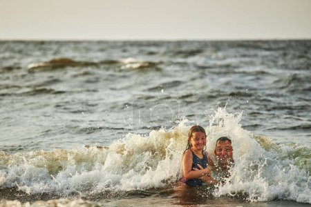 Foto de Niña y su padre jugando con olas en el mar. Vacaciones familiares de verano. Chico salpicando juguetonamente con olas junto con su padre. Saltando en olas marinas. Vacaciones de verano en la playa. Salpicaduras de agua. Viaje durante el concepto de verano - Imagen libre de derechos