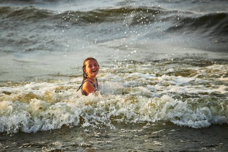 Foto de Niña jugando con olas en el mar. Chico salpicando juguetonamente con olas. Niño saltando en olas marinas. Vacaciones de verano en la playa. Salpicaduras de agua. Viaje durante el concepto de verano - Imagen libre de derechos
