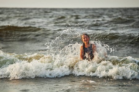 Foto de Niña jugando con olas en el mar. Chico salpicando juguetonamente con olas. Niño saltando en olas marinas. Vacaciones de verano en la playa. Salpicaduras de agua. Viaje durante el concepto de verano - Imagen libre de derechos