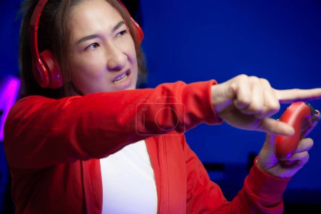 Photo for Excited Asian women gamer with headphone holding joystick playing video game online. professional streamers gaming Get angry and challenge streaming on social playing game. Cyber Neon Lights Style - Royalty Free Image