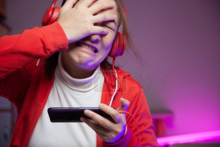 Photo for Asian women gamer with headphone playing mobile game on the smartphone online. professional streamers gaming streaming on social playing game having regrets losing the game. Cyber Neon Lights Style - Royalty Free Image