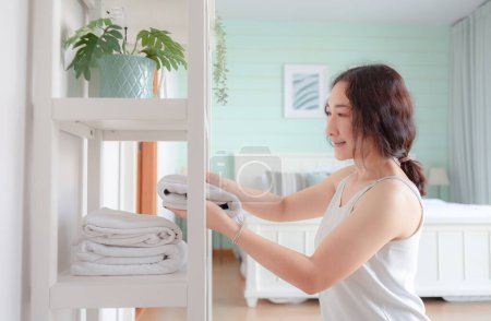 Photo for Positive Asian woman housewife tidying modern home. Happy woman doing domestic chores. Asian housewife folding clothes in the closet. - Royalty Free Image