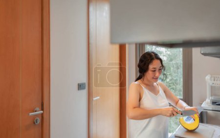 Téléchargez les photos : Femme asiatique positive femme au foyer cuisine des aliments végétariens sains à la maison de la cuisine. Une femme heureuse qui fait des tâches domestiques. Femme asiatique couper des légumes sur la table de cuisine - en image libre de droit