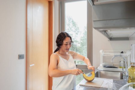 Photo for Positive Asian woman housewife cooking healthy vegetarian food at kitchen home. Happy woman doing domestic chores. Asian woman cut vegetables on kitchen table - Royalty Free Image