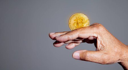 Téléchargez les photos : La main des personnes âgées tient une pièce d'or Bitcoin. La monnaie crypto-monnaie Confiance financière des personnes âgées après la retraite concept. - en image libre de droit