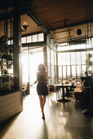 Téléchargez les photos : Portrait d'une femme bouclée marchant dans un restaurant rétroéclairé. Photo de haute qualité - en image libre de droit