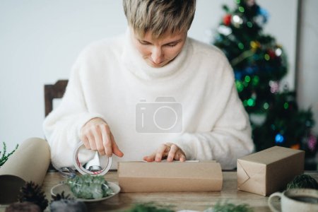 Photo for Woman in Santa hat wrapping christmas presents with eco materials at home - Royalty Free Image